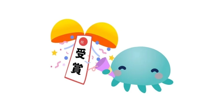 青い可愛いキャラクターがパーティーポッパーを鳴らし、開いたカプセルから「祝 受賞」のバナーと紙吹雪が出ているお祝いのイラスト