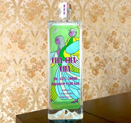 レトロな花柄の壁紙を背景に、CHA-CHA-CHAジャパニーズクラフトジンのボトルが写っています。緑色のラベルには、鮮やかな色使いでダンスをする男女のイラストが描かれており、目を引くデザインです。