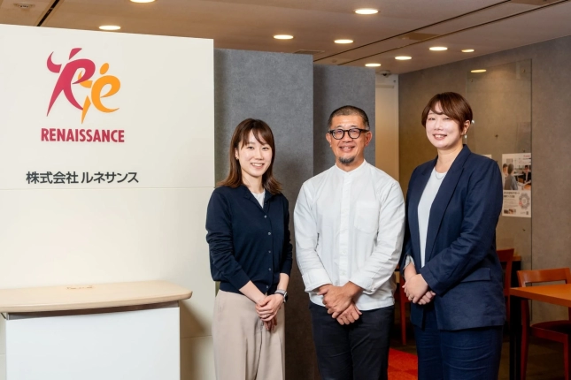 オフィス内で笑顔で立つ3人のビジネスパーソン